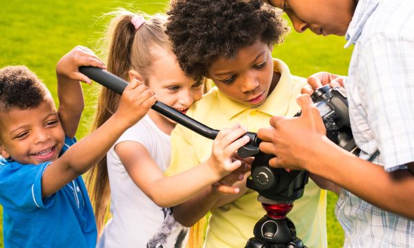 Four nice children are playing with camera and going to take a picture.